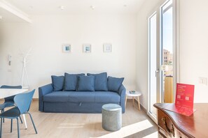 A modern living room with a blue sofa, a round wicker ottoman, and a small side table. - Igiea Florio Sea View by Wonderful Italy (Palermo)