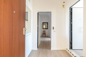 A hallway with a wooden door on the left, a white door on the right, and a mirror on the wall. - Igiea Florio Sea View by Wonderful Italy (Palermo)