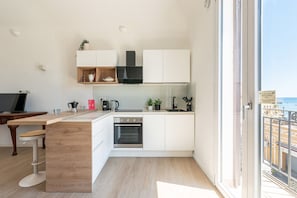 A modern kitchen with white cabinets, a wooden countertop, a built-in oven, and a view of the city through a large window. - Igiea Florio Sea View Terrace by Wonderful Italy (Palermo)