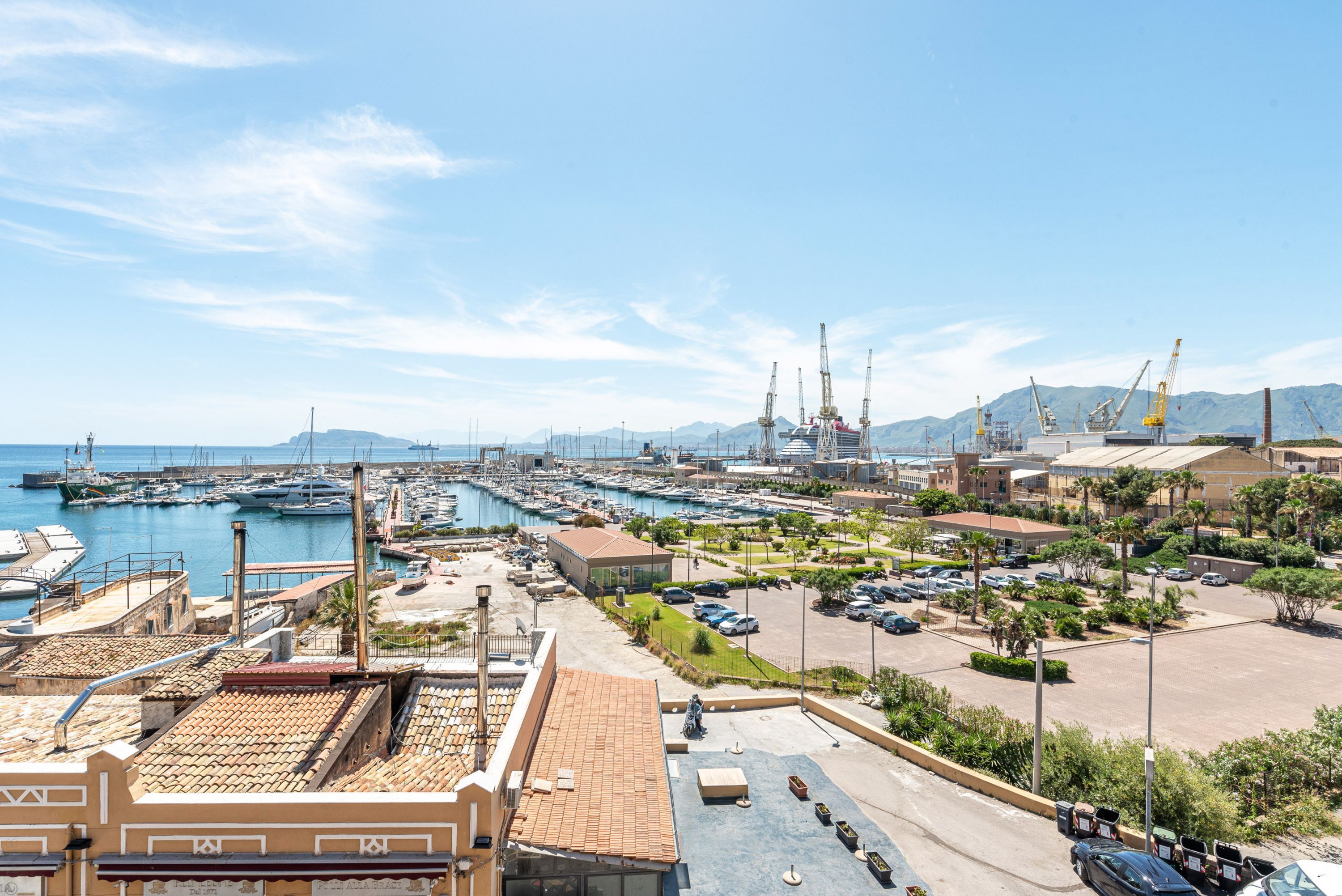 A marina with boats, a parking area, and buildings with Mediterranean architecture.