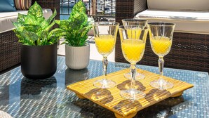 En balkon med fletningsmøbler, plantekasser og et fad med appelsinjuice.