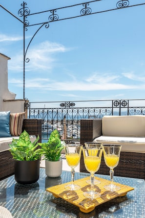 Ein Balkon mit Korbmöbeln, Blumentöpfen und einem Tablett mit Orangensaftgläsern.