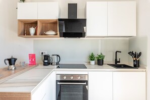 Eine moderne Küche mit weißen Schränken, einer schwarzen Dunstabzugshaube, einem eingebauten Backofen, einer Kaffeemaschine und einem Spülbecken mit Besteck.