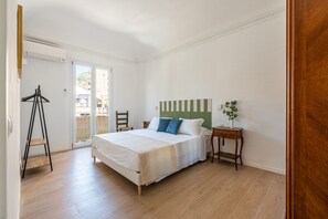 Ein Schlafzimmer mit Bett, Nachttisch, Stuhl, Kleiderhaken und Blick durch eine Tür.