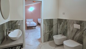 A bathroom with a white sink, bidet, and toilet, marble walls, and a visible bedroom with a bed and a nightstand. - B&b Villa Ravenna (Ravenna)
