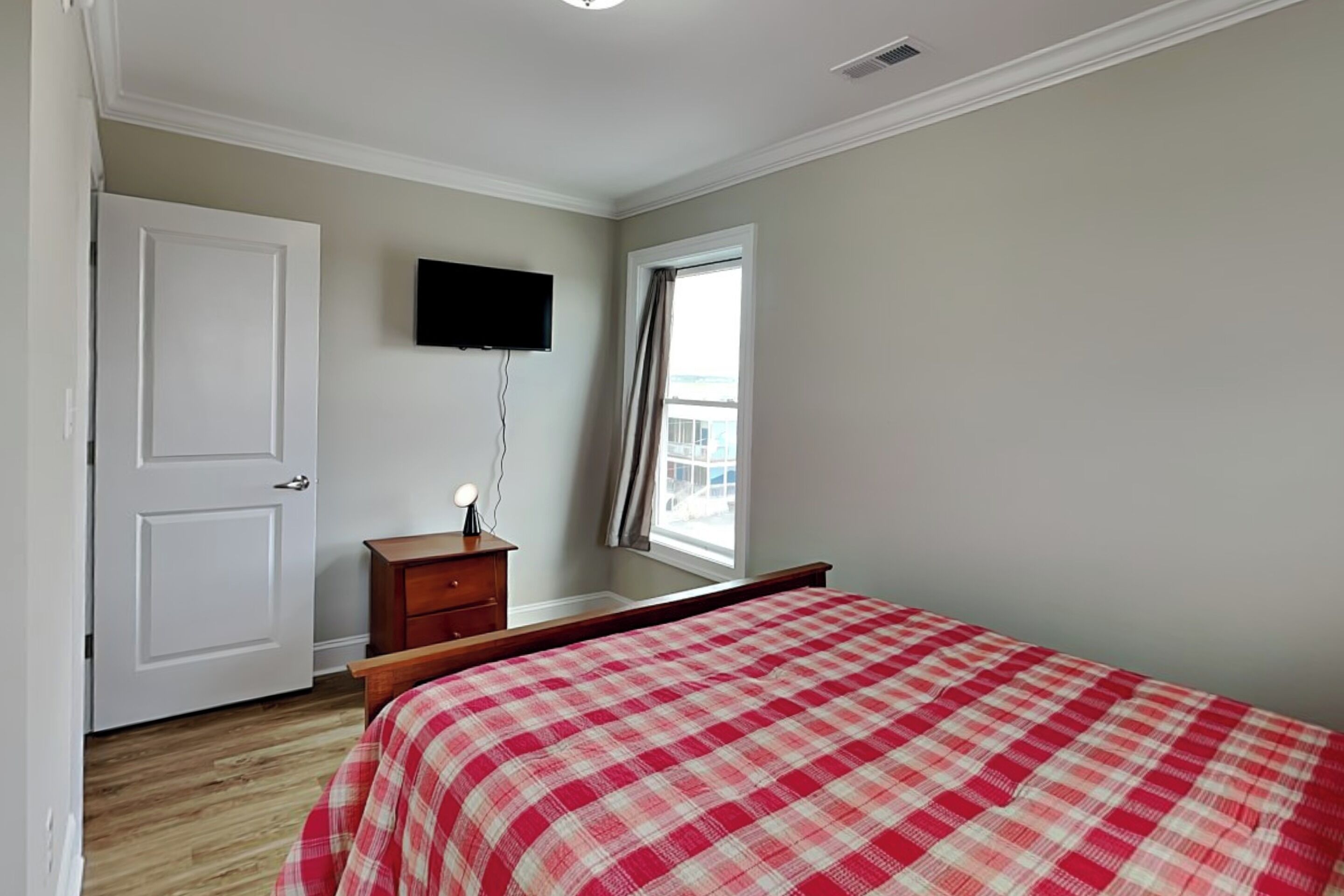 A bedroom with a bed, a television mounted on the wall, a window with curtains, and a door.