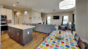 Una cocina moderna con una isla central, comedor con mantel colorido y sala de estar con televisor.