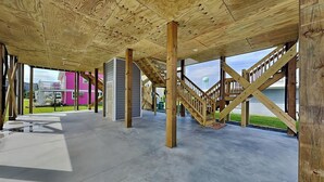 An open-plan interior with exposed wooden beams, a concrete floor, and a staircase leading to an upper level. - Sound Side Sunset (Holly Ridge)