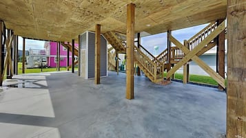Un interior de planta abierta con vigas de madera a la vista, suelo de hormigón y una escalera que sube a un nivel superior.