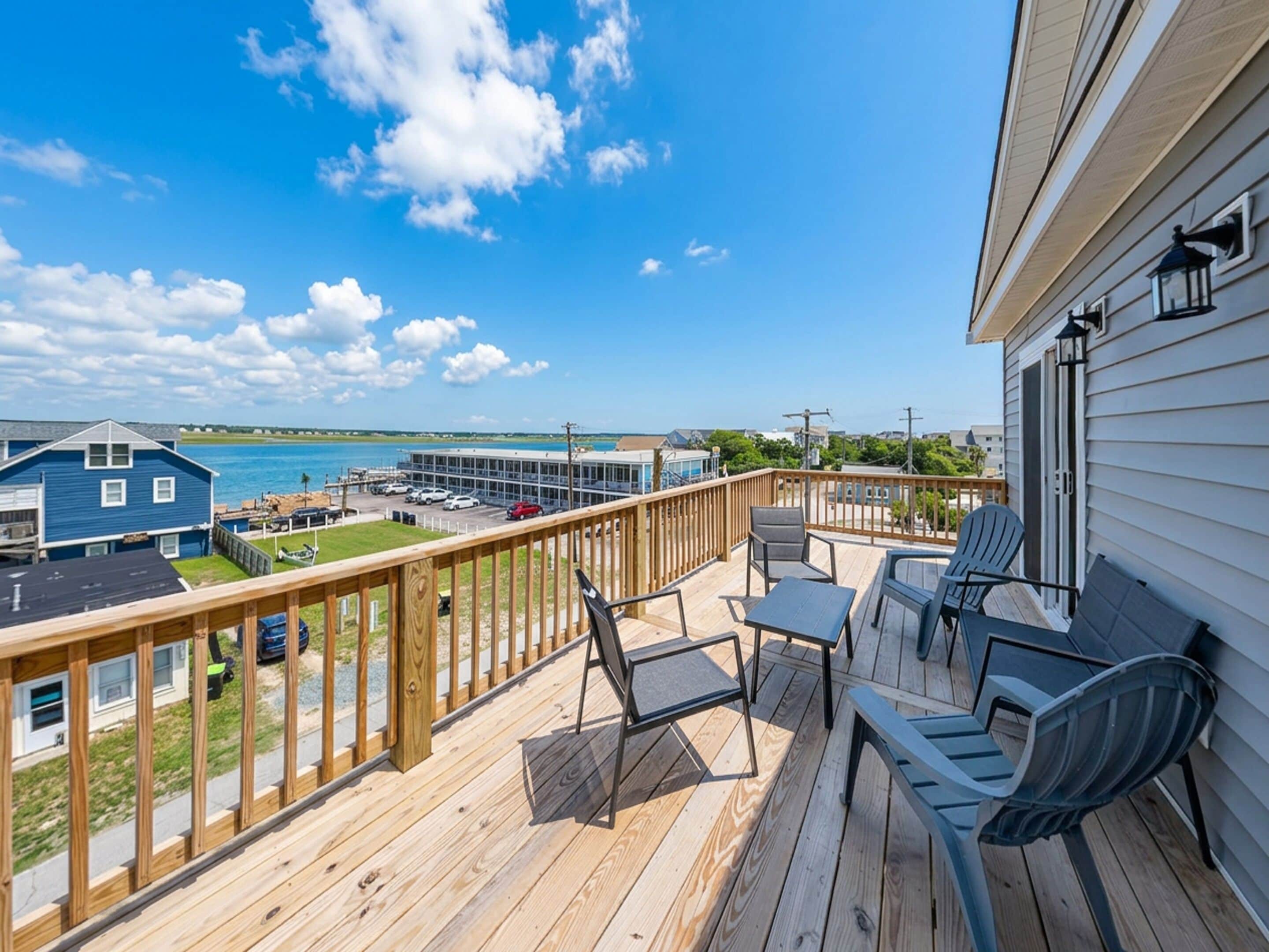 A wooden deck with outdoor furniture, overlooking a body of water and buildings.
