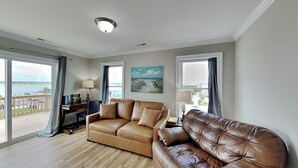 A living room with a brown leather sofa, a desk, and a painting of a beach scene. - Sound Side Sunset (Holly Ridge)