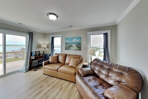 Ein Wohnzimmer mit einem braunen Ledersofa, einem Schreibtisch und einem Bild von einer Strandlandschaft.