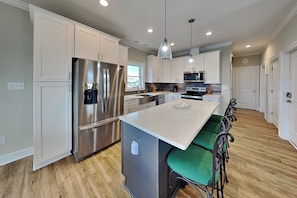 A modern kitchen with stainless steel appliances, white cabinetry, and a central island with bar stools. - Sound Side Sunset (Holly Ridge)