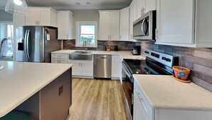 A modern kitchen with white cabinets, stainless steel appliances, and a large island. - Sound Side Sunset (Holly Ridge)