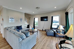 A living room with a large grey sofa, a coffee table, a TV, and a staircase leading to another level. - Sound Side Sunset (Holly Ridge)