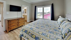 A bedroom with a bed, dresser, TV, and a window with curtains. - Sound Side Sunset (Holly Ridge)
