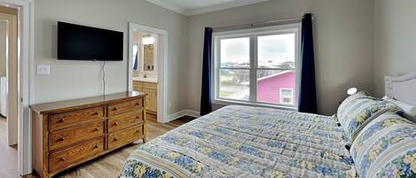 A bedroom with a bed, dresser, TV, and a window with curtains.