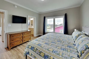 Ein Schlafzimmer mit Bett, Schminktisch, Fernseher und einem Fenster mit Vorhängen.