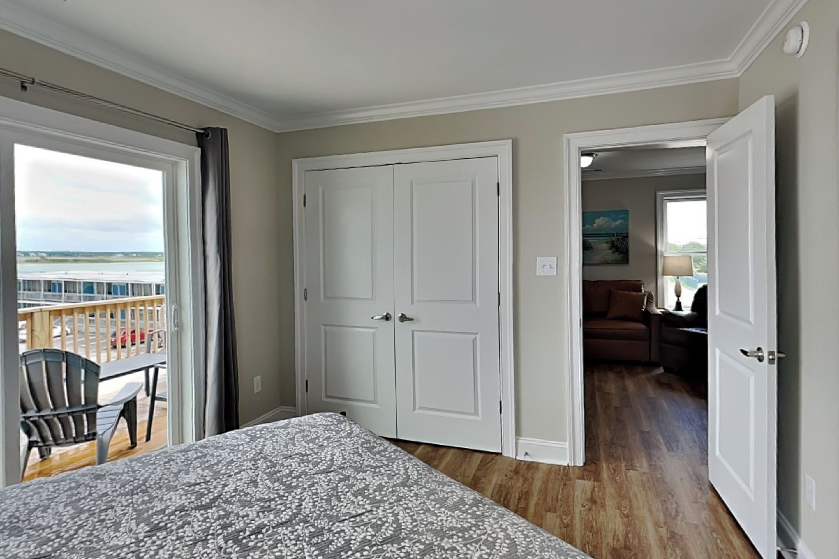 A hotel room with a balcony, a bed, a door leading to another room, and a view of the beach.
