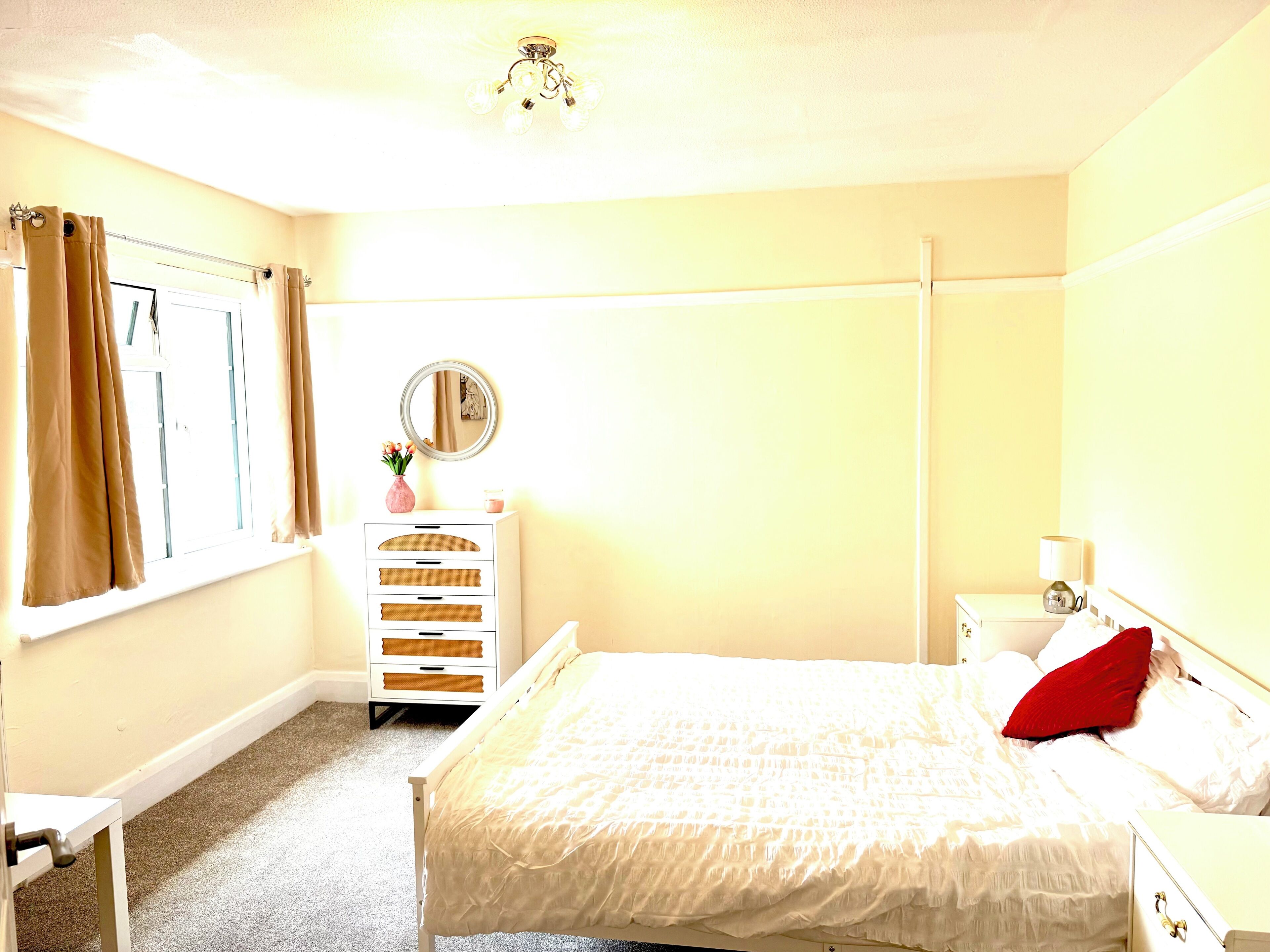 Un dormitorio con cama, cómoda, espejo y ventana con cortinas.