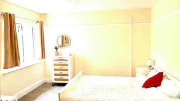 Un dormitorio con cama, cómoda, espejo y ventana con cortinas.