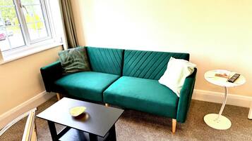 A teal sofa with a striped pillow, a small table with a bowl, and a round side table with a remote control.