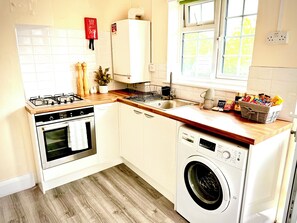 Une cuisine compacte équipée d’une cuisinière à gaz, d’un four, d’un évier et d’un lave-linge encastré.