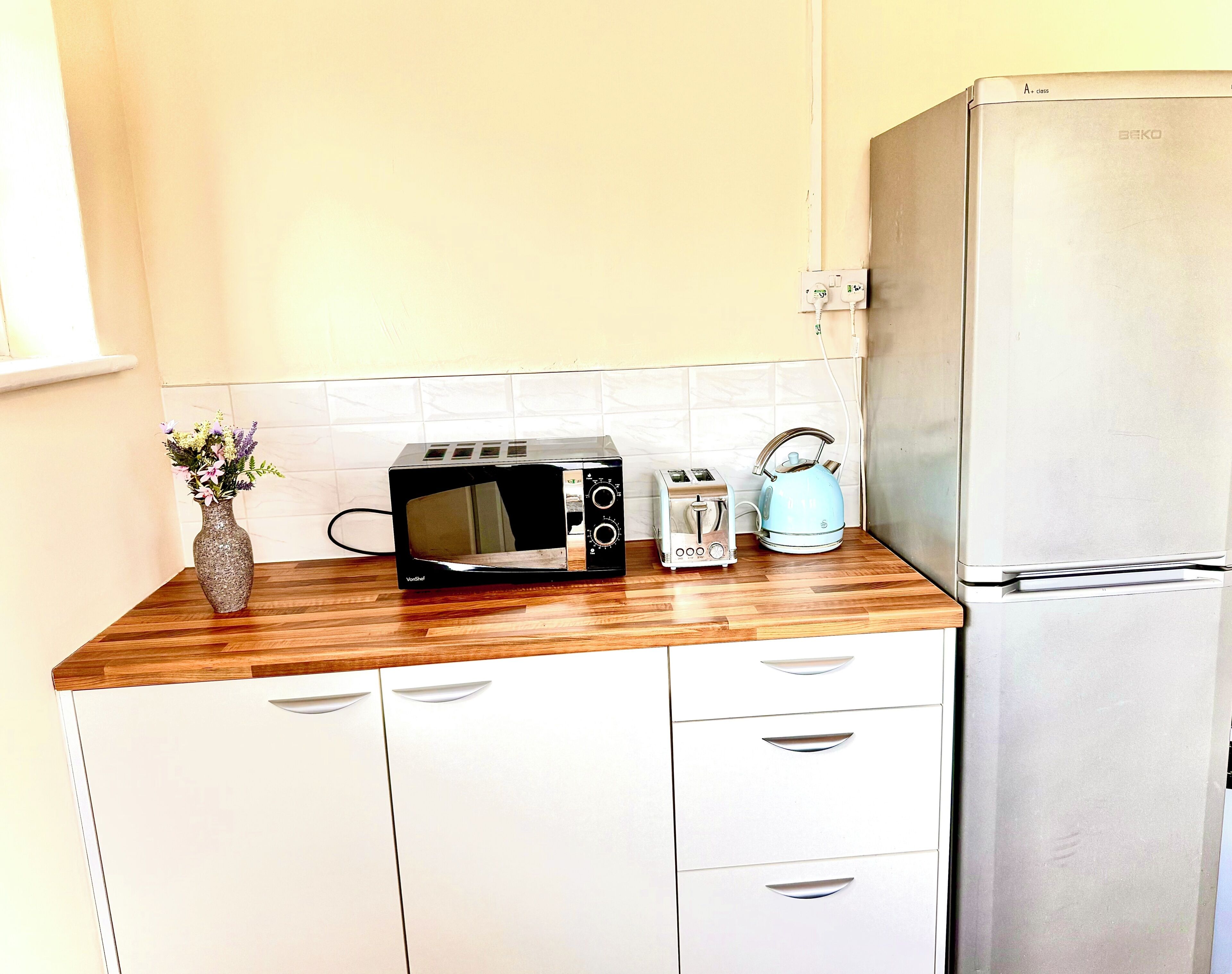 A kitchen with a microwave, toaster, kettle, and a refrigerator.