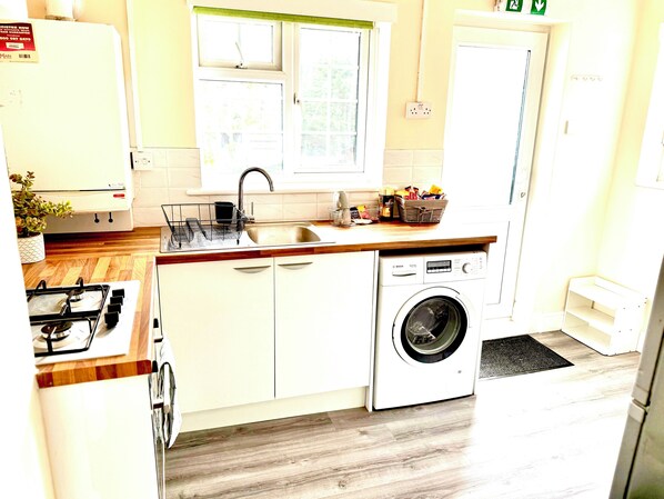 A compact kitchen with a gas stove, sink, and a front-loading washing machine.