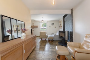 Een woonkamer met een bank, een televisie, een open haard en een eethoek met een spiegel en een bloemenvaas.