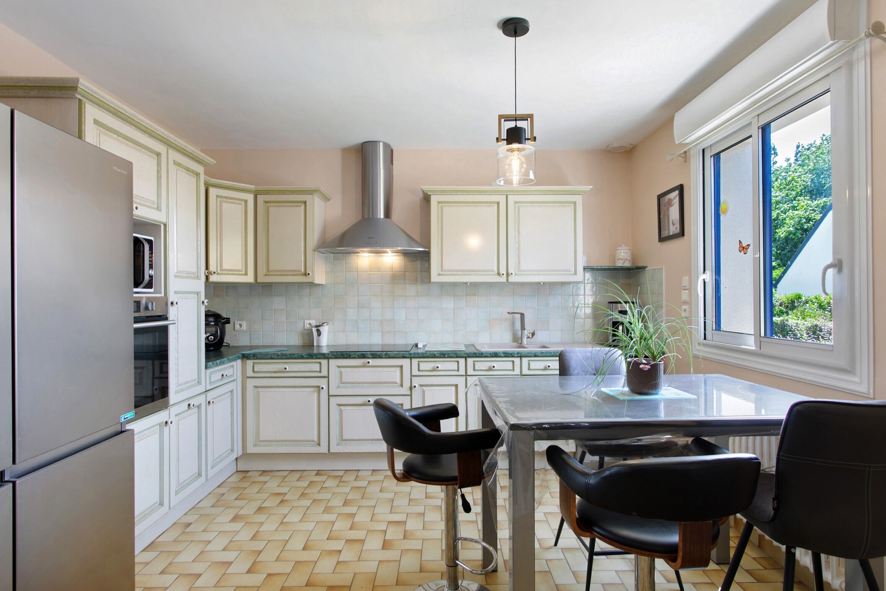 A kitchen with white cabinets, a stainless steel range hood, a marble countertop, and a dining area with a table and chairs.