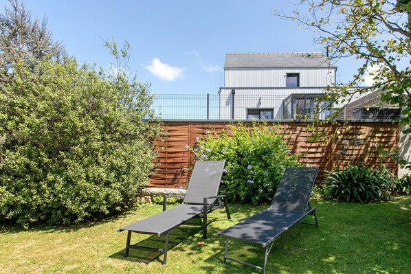 Een achtertuin met twee loungesteunen, een houten omheining en een gebouw op de achtergrond.