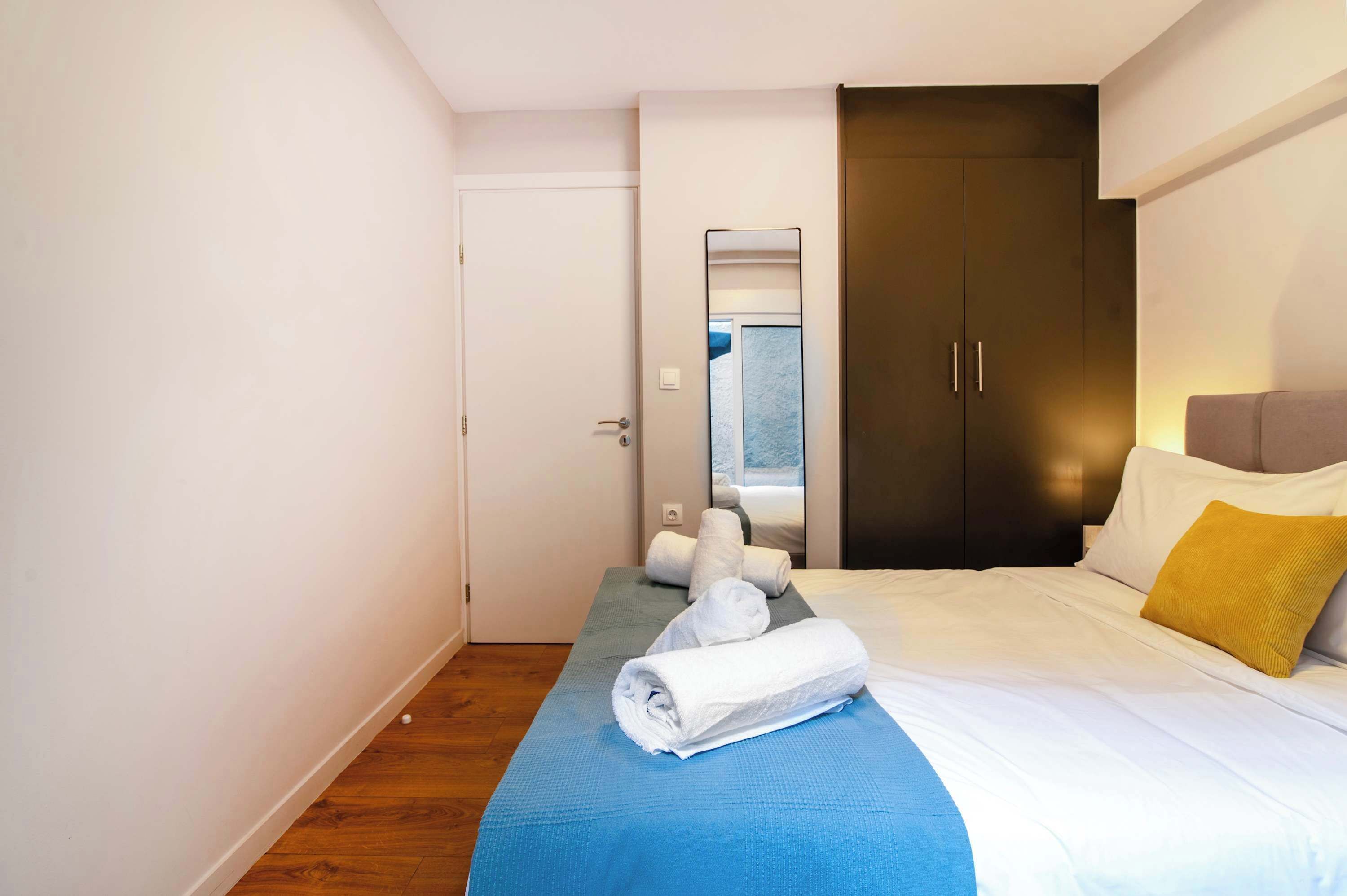 Una camera d'albergo con un letto, una coperta blu, un cuscino bianco e un cuscino giallo, su un pavimento di legno.