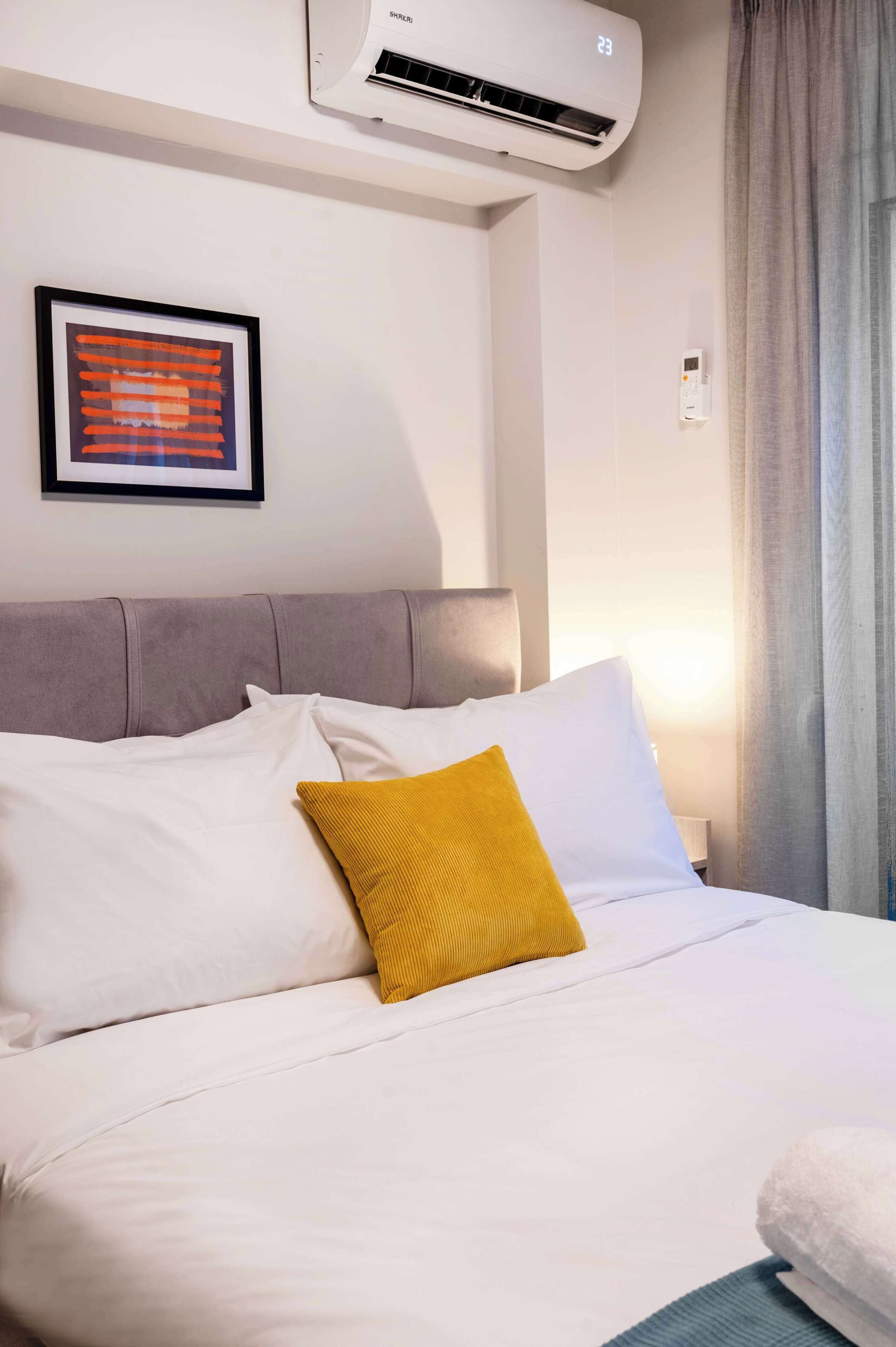 Ett hotellrum med en säng, ett inramat konstverk på väggen och en luftkonditioneringsanläggning ovanför sängen.