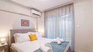 Quarto de hotel com cama, mesa de cabeceira, ar condicionado e janela com cortinas.