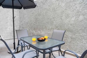 Eine Terrasse im Freien mit Tisch, Stühlen, Sonnenschirm und einer Schüssel Croissants und Orangensaft.