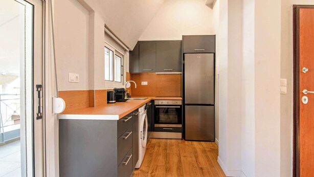 Cocina compacta con armarios grises, un refrigerador de acero inoxidable, horno empotrado y lavadora.