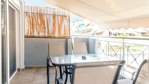 Un balcón con una mesa y sillas, una cortina a rayas y vistas de edificios al fondo.