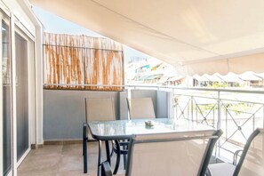 Ein Balkon mit Tisch und Stühlen, einem gestreiften Vorhang und Blick auf Gebäude im Hintergrund.