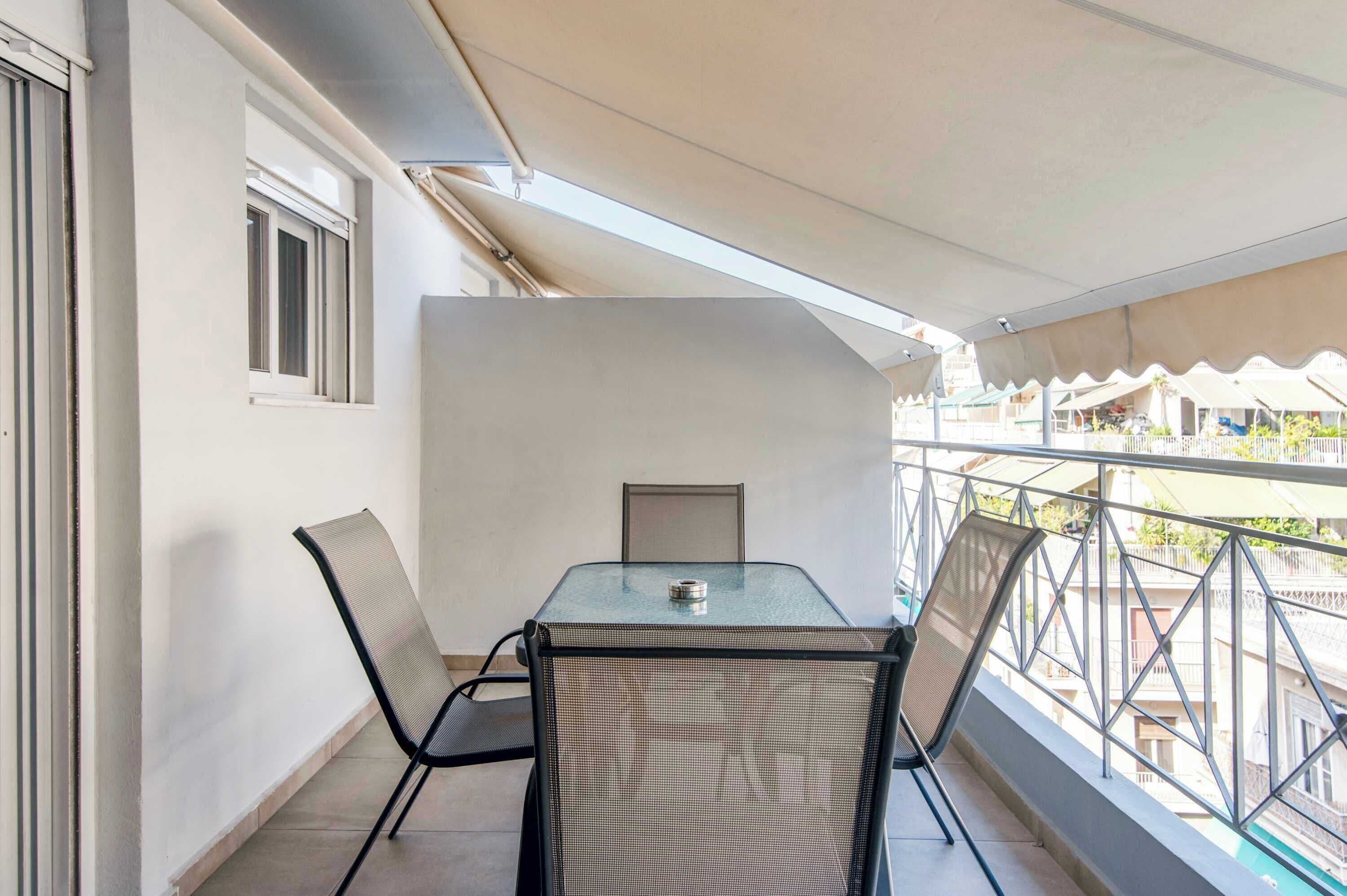 A balcony with a table and chairs, a window, and a view of buildings.