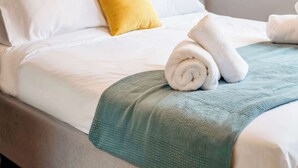 A neatly made bed with white linens, a yellow pillow, and rolled towels. - Modern Athens Apartment Near Attractions (Athens)