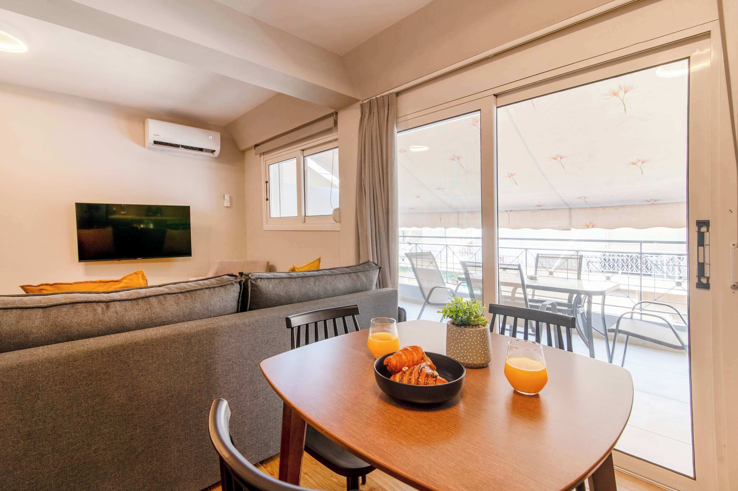 A modern living area with a sofa, dining table, and a TV mounted on the wall.