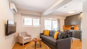 A modern living room with a grey sofa, a small round table, and a TV mounted on the wall. - Modern Athens Apartment Near Attractions (Athens)