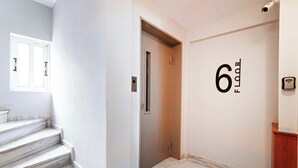 A clean, modern hallway with marble stairs leading to an elevator, a wall-mounted number indicating the floor, and a security camera. - Modern Athens Apartment Near Attractions (Athens)