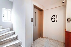 Ein sauberer, moderner Korridor mit Marmorstufen, die zu einem Aufzug führen, einer an der Wand befestigten Zahl, die die Etage angibt, und einer Überwachungskamera.