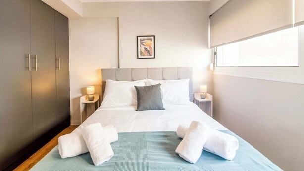 A hotel room with a bed, a headboard, two bedside tables with lamps, a wardrobe, and a window. - Modern Athens Apartment Near Metro Station (Athens)