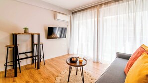 A modern living room with a flat-screen TV, a sofa, a coffee table with a bowl and glass, and a small stool. - Modern Athens Apartment Near Metro Station (Athens)