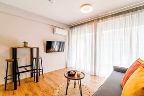 A modern living room with a flat-screen TV, a sofa, a coffee table with a bowl and glass, and a small stool. - Modern Athens Apartment Near Metro Station (Athens)