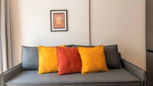 A grey sofa with three cushions in yellow, red, and grey, and a framed abstract artwork on the wall. - Modern Athens Apartment Near Metro Station (Athens)