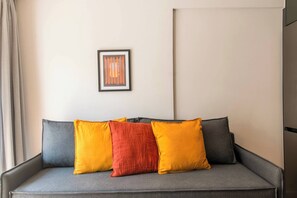 A grey sofa with three cushions in yellow, red, and grey, and a framed abstract artwork on the wall. - Modern Athens Apartment Near Metro Station (Athens)